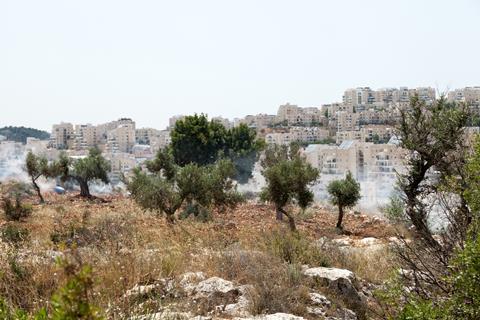 Photo showing Tear gas clouds spreading in the Palestinian field on the lands of Bil in village in the west bank, with Jewish settlement on the Palestinian occupied territories in the background.